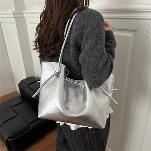 Metallic silver large tote bag with knot detail shown on a model in a minimalist setting