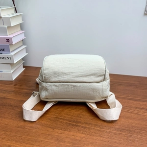 Dettaglio mini zaino in nylon stropicciato crema con spallacci in tessuto su legno