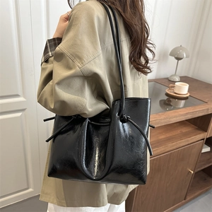 Glossy black leather tote bag with drawstring detail worn by a model in a warm interior