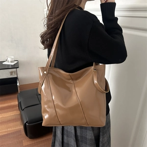 Sac fourre-tout en similicuir marron brillant avec rivets argentés porté par mannequin