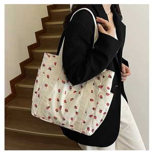 Detailed close-up of a white corduroy tote bag with red strawberry prints worn with a blazer
