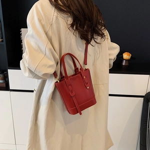 Deep red leather bucket bag with top handle and crossbody strap in a modern room setting