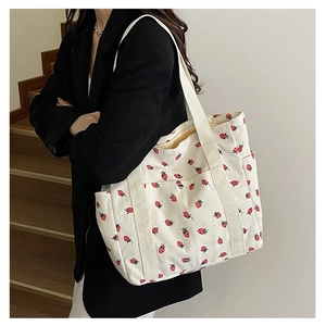 Close-up of white corduroy tote bag featuring red strawberry prints and functional side pockets