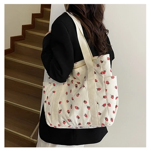 Detail of white corduroy tote bag featuring red strawberry patterns and wide shoulder strap