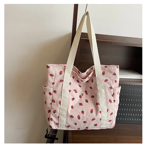 Detail of pink corduroy tote bag with strawberry print and white canvas strap on a rack