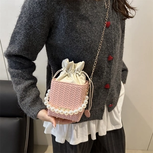 Pink woven bucket bag with pearl handle and golden chain strap shown on model
