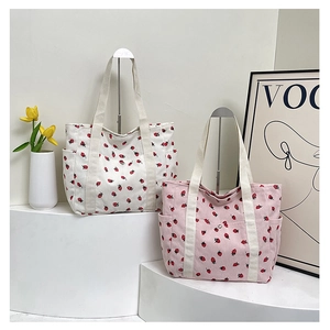 Detail of corduroy strawberry tote bags with side pockets and magnetic snap on white stand