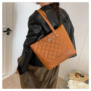 Detail of brown quilted tote bag with silver bow charm and slim straps on model