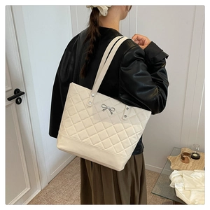 Detail of quilted beige tote bag with a silver bow buckle worn on the shoulder
