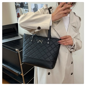 Close-up of quilted black tote bag with gold bow detail shown in a casual lifestyle setting