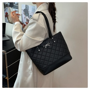 Side view of a large black quilted tote bag with silver bow charm on a model