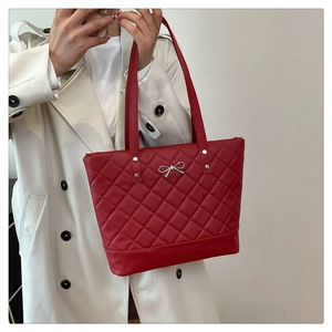 Close-up of red quilted tote bag with silver bow charm on a model in trench coat