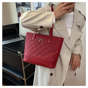 Detail of red quilted tote bag with silver bow buckle worn with a beige trench coat
