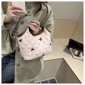 Pink quilted tote bag with black bow embroidery and brown trim held by a model