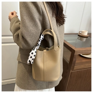 Détail du sac seau en cuir kaki avec foulard à pois sur la poignée et décor raffiné