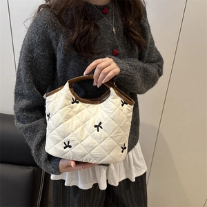 White quilted tote bag with black bow embroidery and contrasting brown handles