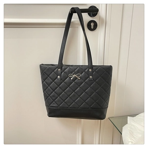 Detail of quilted leather tote bag with golden bow hardware and rivet accents
