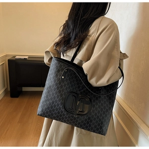 Détail d'un sac cabas noir avec motif monogramme M et longues bandoulières en cuir souple