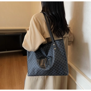 Detail of grey monogram tote bag showing large M logo patch and long black handles