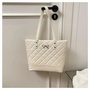 Detail of quilted tote bag in cream with a metal bow accent and long shoulder straps