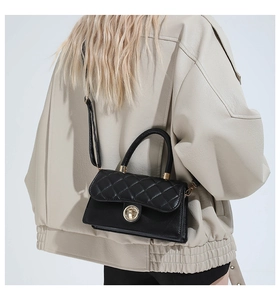 Detalle de bolso bandolera de piel acolchada negra con cierre dorado en una modelo