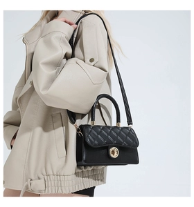 Detalle de bolso acolchado negro con cierre dorado sobre abrigo de cuero beige