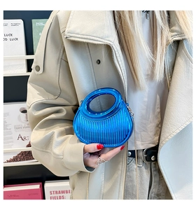Detail of electric blue pleated handbag with gold chain strap held by a model