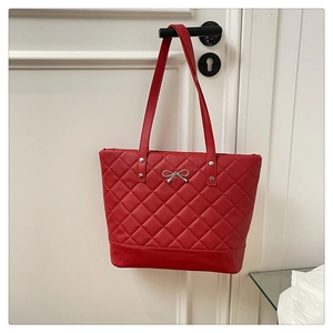 Close-up of red quilted tote bag with silver bow charm and elegant diamond pattern