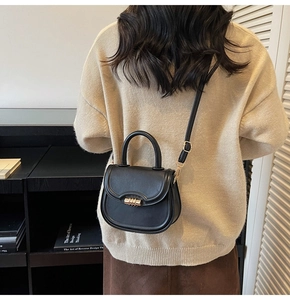 Close-up of black leather saddle bag with gold buckle and adjustable shoulder strap