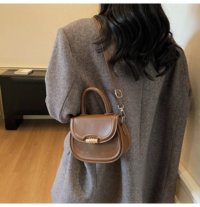 Close-up of brown leather saddle bag with gold metal buckle and adjustable shoulder strap