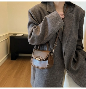 Close-up of a dark brown saddle bag with gold metal twist lock and adjustable strap