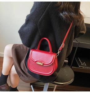 Detailed view of red leather saddle bag featuring gold metal clasp and thin crossbody strap