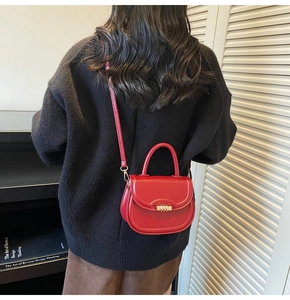 Close-up of a mini bright red saddle bag with gold clasp held by a model in casual wear