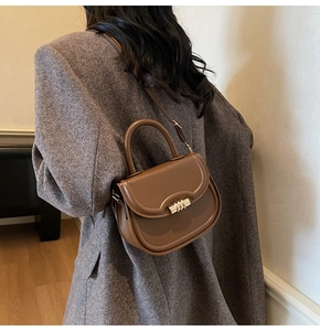 Detailed side view of a brown saddle bag with gold buckle on a model in tweed coat