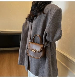 Detail of a caramel brown leather saddle bag with a metallic twist lock on a wool blazer
