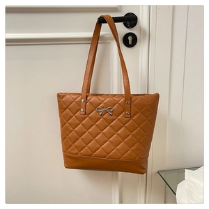 Detailed view of brown quilted tote bag with a small silver metal bow decoration