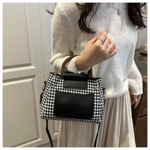 Detail of houndstooth fabric bag with vintage wood grain handle and black leather flap