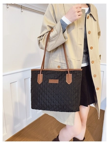 Detail of black quilted tote bag with brown leather straps and fashion label