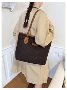 Detail of black quilted tote bag with brown leather handles and brand tag on beige trench