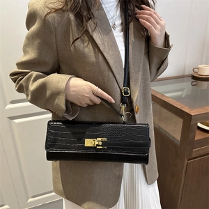 Elegant black crocodile pattern crossbody bag with gold hardware worn by a model in a suit