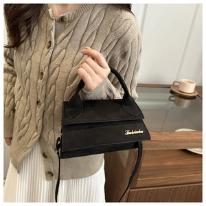Detail of a matte black mini handbag with gold logo and elegant top handle held by hand