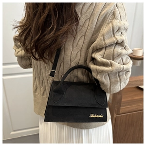 Detail of black suede mini bag with gold logo and elegant adjustable shoulder strap