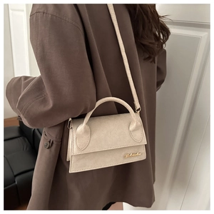 Close-up of beige leather crossbody bag with gold logo on a dark brown blazer