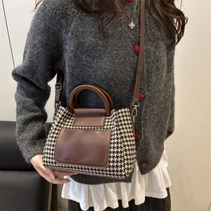 Retro houndstooth handbag with brown leather trim and wooden handle on model shoulder