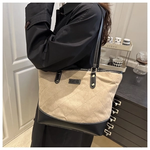 Close-up of quilted beige tote bag with black leather straps worn as a shoulder bag