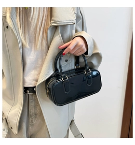 Close-up of black glossy patent leather Boston bag with gold hardware and dual handles
