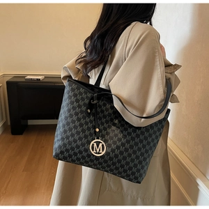Detail of a black tote bag featuring grey M logo prints and a gold M metal charm