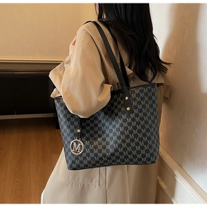 Gros plan du sac cabas noir avec motif M gris et breloque logo M en métal doré