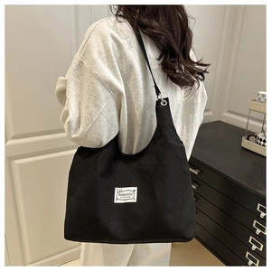 Detail of a black corduroy tote bag with a white fashion woven label for daily use