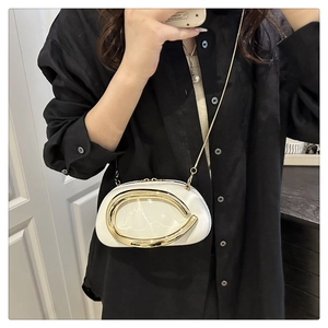 Detail of white glossy crossbody bag with golden C-shaped metal hardware and chain strap